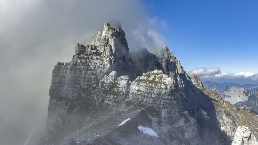 Cime montuose rocciose avvolte dalle nuvole sotto un cielo blu.