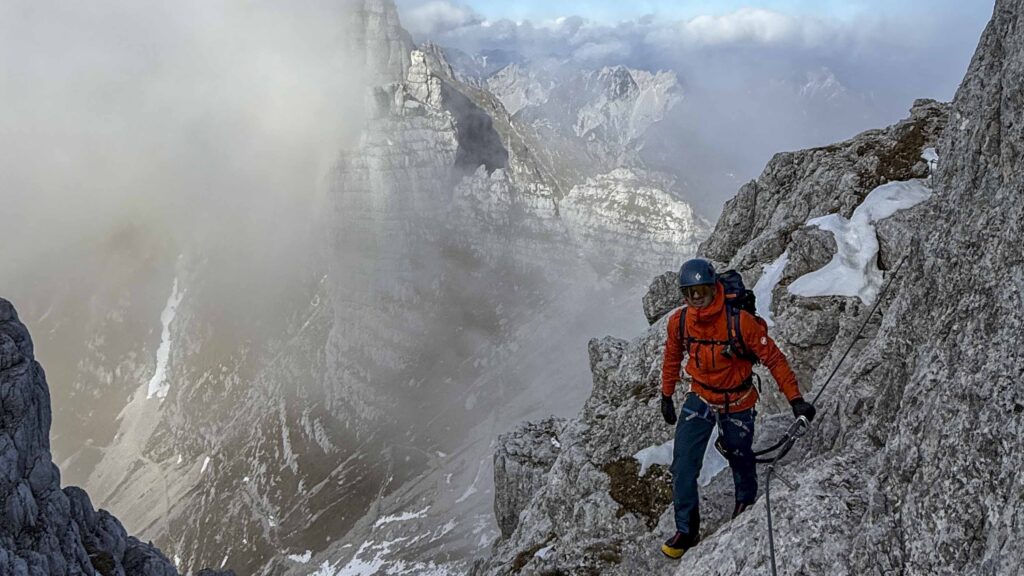 Alpinista esperto su una via ferrata con nebbia e montagne sullo sfondo.