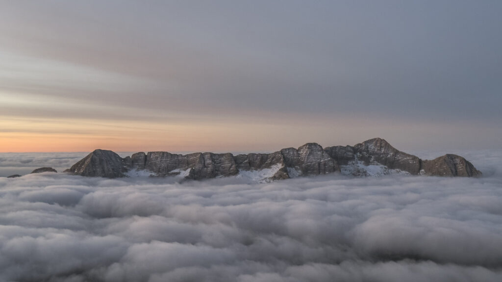 Cima di montagna innevata che emerge da un mare di nuvole al tramonto.