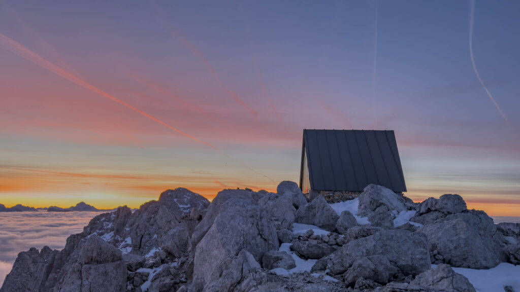 Rifugio montano su rocce innevate al tramonto.