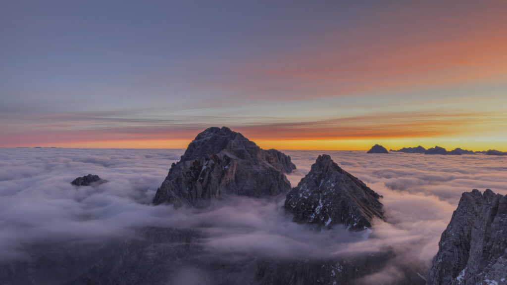 Montagne rocciose emergono da un mare di nuvole al tramonto.