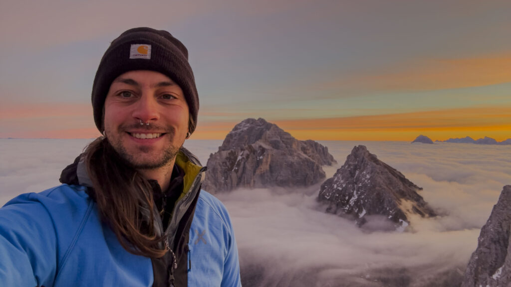Uomo sorridente in montagna sopra le nuvole all'alba.