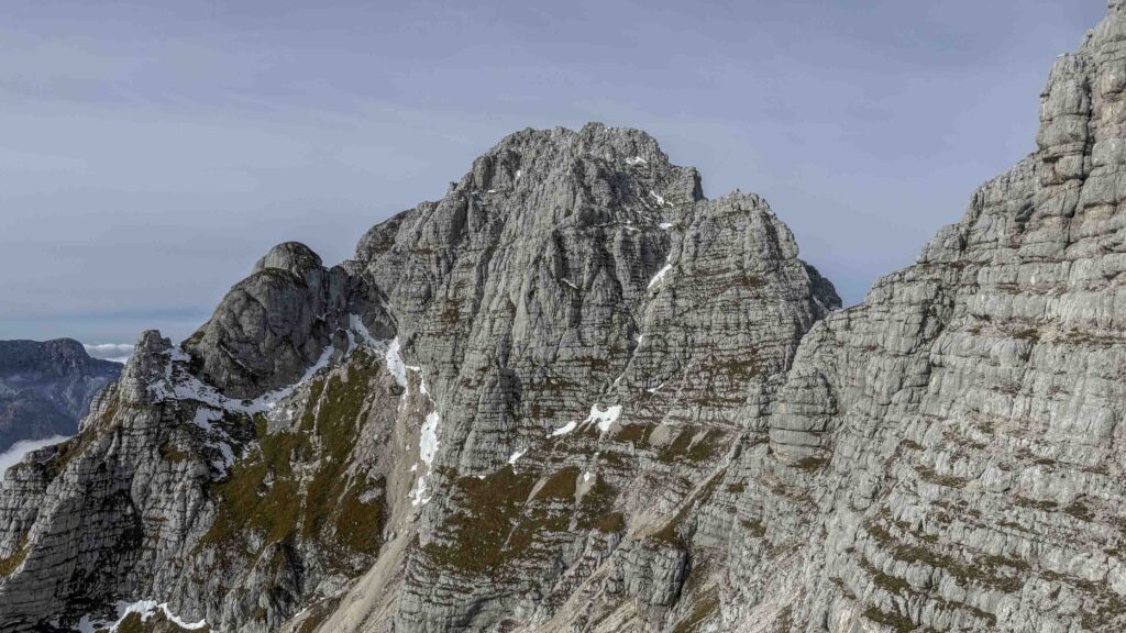 Cima rocciosa frastagliata con neve e vegetazione.